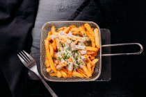 Fresh delicious French fries sprinkled with chopped potherbs with sauce in wire fryer basket on slate — Stock Photo