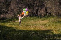Elementary age boy running on meadow with balloons — Stock Photo