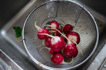 Washing fresh radishes in strainer under tap — Stock Photo