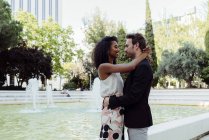Charming multiracial couple embracing near fountain in city park — Stock Photo