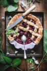 Colocação plana de torta de cereja assada com crosta de treliça servida em mesa rústica com folhas verdes — Fotografia de Stock