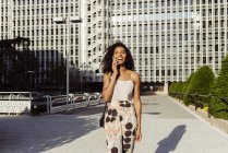 Elegante donna afro-americana che parla su smartphone mentre cammina per strada in una giornata di sole — Foto stock