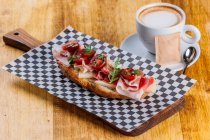 Sandwich with bacon and cherry tomatoes on wooden table with cup of cappuccino — Stock Photo