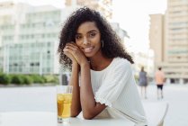 Charming African-American woman sitting with glass of beverage in outdoor cafe — Stock Photo