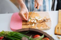 Cebolla de primavera de corte femenino con cuchillo en tabla de cortar en la cocina - foto de stock