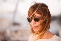 Женщина с летящими светлыми волосами в современных солнцезащитных очках смотрит на улицу — стоковое фото