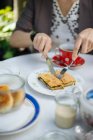 Frauenhände schneiden Stück Teig auf Teller mit Messer und Gabel auf Gartentisch — Stockfoto