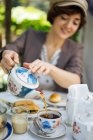 Woman pouring tea in vintage porcelain cup on garden table with pastry — Stock Photo