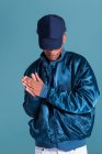 Trendy uomo etnico indossa giacca bomber blu lucido e cappuccio sullo sfondo blu — Foto stock