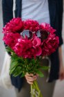 Nahaufnahme einer Frau, die einen Strauß rosa Pfingstrosen mit Sonnenbrille an der Spitze hält — Stockfoto