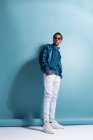 Portrait of black man in blue bomber jacket and sunglasses standing on blue background — Stock Photo