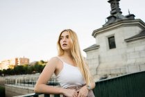Young woman leaning on bridge railing and looking away — Stock Photo