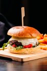 Close-up of fresh burger with meat patty and vegetables placed on wooden board with French fries on wooden board — Stock Photo