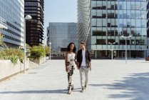 Glückliches multiethnisches Paar lächelnd und Händchenhaltend beim gemeinsamen Gehen auf der modernen Stadtstraße — Stockfoto