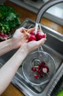 Woman washing fresh radishes in kitchen sink — Stock Photo