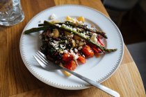 Patata arrosto brillante saporita con verdure che giacciono con fagiolini e forchetta su piatto bianco con ornamento su tavolo di legno dall'alto — Foto stock