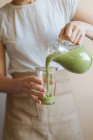 Mains féminines versant smoothie vert sain de tasse mélangeur dans le verre — Photo de stock