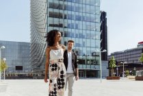 Glückliches multiethnisches Paar lächelnd und Händchenhaltend beim gemeinsamen Gehen auf der modernen Stadtstraße — Stockfoto
