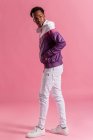 Стильний хіпстер в барвистій куртці з навушниками, що стоять на рожевому фоні — стокове фото