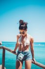 Молода дівчина в літньому одязі спирається на дерев'яний поручень на пляжі — стокове фото