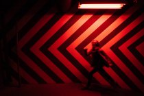 Вид збоку розмита фігура чоловічої статі, що йде в тунелі в протилежному напрямку до великих червоних і чорних стріл на стіні, освітлених червоними лампами — стокове фото