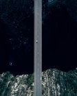 Luftaufnahme eines Kleinwagens, der auf der leeren Straße der Brücke über die dunkle Meeresbucht mit felsiger Küste fährt — Stockfoto