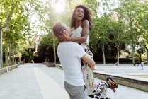 Uomo sollevamento donna ridente mentre in piedi sul vicolo del parco nella giornata di sole — Foto stock