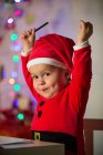 Glückliches kleines Kind in Weihnachtskleidung blickt in die Kamera — Stockfoto
