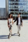 Happy multiracial couple smiling and holding hands while walking on modern city street together — Stock Photo