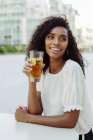 Charmante femme afro-américaine tenant un verre de boisson dans un café extérieur — Photo de stock