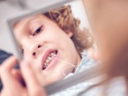 Menino segurando espelho e olhando em reflexão enquanto arrancando dente com fio — Fotografia de Stock