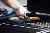 Recorte de hombre asando empanadas de carne con queso en parrilla humeante a la luz del sol - foto de stock