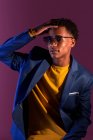 Молодой привлекательный афроамериканец в свитере и куртке с рукой на волосах, смотрящий в камеру при свете фонаря — стоковое фото