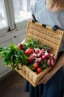 Erntefrau in Hemd und Rock hält in der Hand Korb mit offenem Deckel voller heller frischer Tomaten, Paprika, Rettich und Kartoffeln — Stockfoto