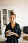 Retrato de jovem mulher em xadrez camisa de pé com caneca de café em casa — Fotografia de Stock