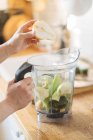Mains féminines mettant poire dans un bol mélangeur pour smoothie vert — Photo de stock