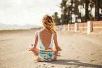 Вид ззаду тонка жінка в барвистому купальнику сидить на піску і дивиться в сторону — стокове фото