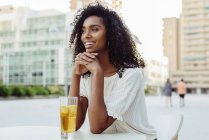 Encantadora mujer afroamericana sentada con un vaso de bebida en la cafetería al aire libre - foto de stock