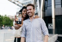 Happy couple posing for selfie while standing on background of modern city — Stock Photo