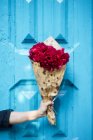 Mano che tiene vivido bouquet di peonie rosa in carta da regalo davanti alla porta di legno blu — Foto stock