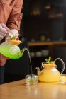 Кукурудзяний чоловік, який подає творчий коктейль зі скляного горщика з фруктами зверху в невелику скляну чашку на столі — стокове фото