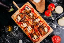Pizza mit Käse, Sauce und geschnittenen Auberginen auf Holzbrett auf dunklem Tisch — Stockfoto