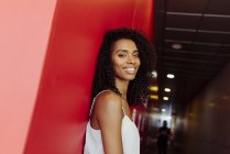 Улыбающаяся афроамериканка в элегантном наряде, стоящая на красном фоне — стоковое фото