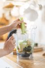 Frauenhände legen Sellerie in Mixer-Schüssel für grünen Smoothie — Stockfoto