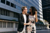 Laughing multiracial couple in sunglasses walking on city street together — Stock Photo