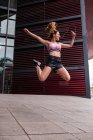 Захоплена м'язиста жінка в спортивному одязі щасливо стрибає з руками на тротуарній вулиці — стокове фото
