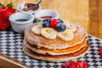 Delicious fried fluffy pancakes with icing sugar and fresh berries served for breakfast on checkered napkin — Stock Photo
