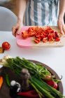 Крупним планом Жіночі руки тримають розрізану дошку з нарізаним червоним перцем і помідорами на кухні — стокове фото