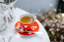 Red ceramic polka-dotted mug of tea on saucer on garden table — Stock Photo