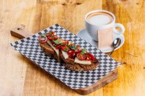 Brown bread sandwich with cheese and tomatoes and cup of cappuccino on wooden table — Stock Photo